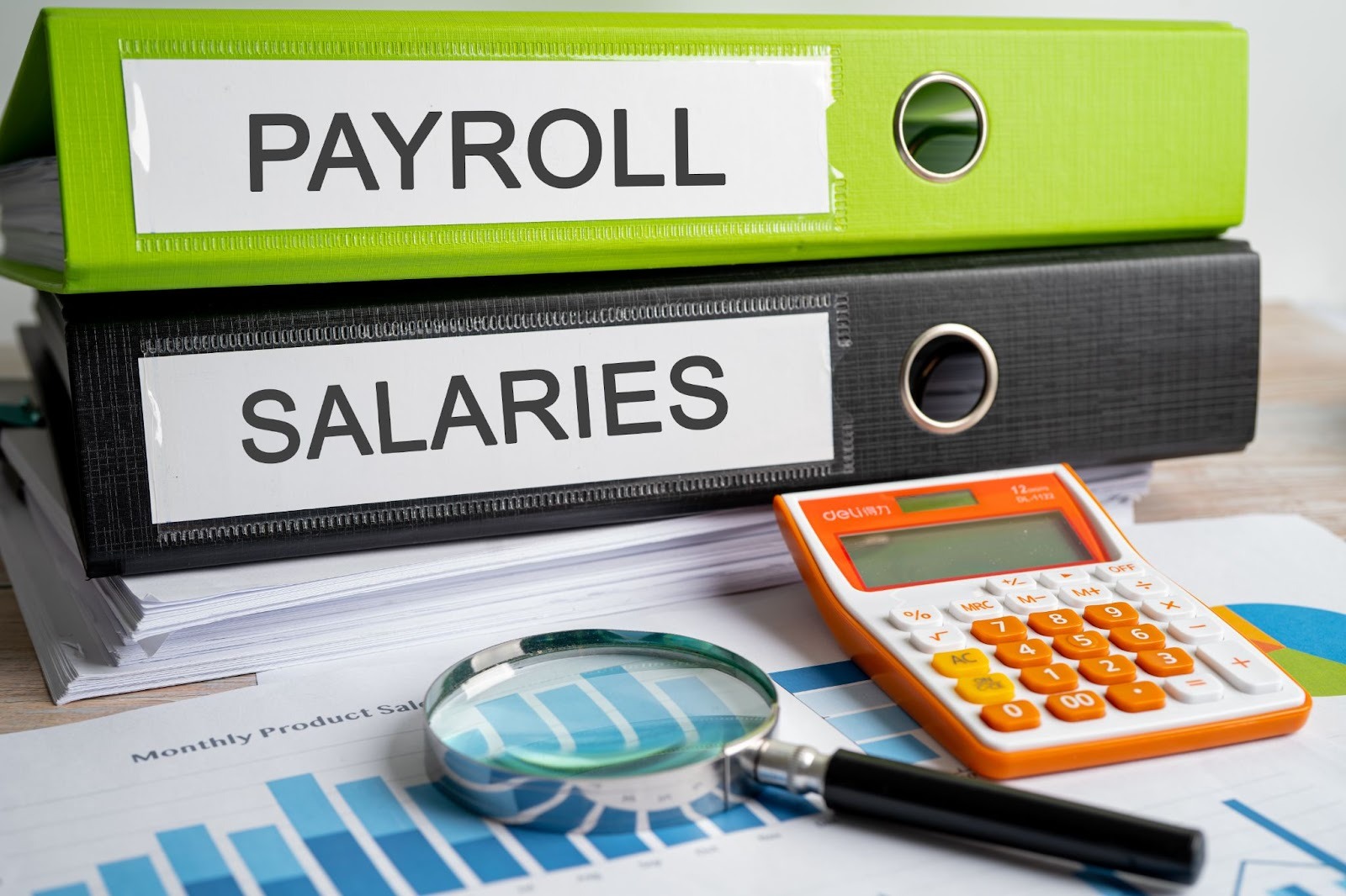 Business payroll and salary documents in binders alongside financial reports with charts and data analysis