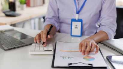 Closeup on a woman with a blue badge performing accounting services with a calculator and notepad.