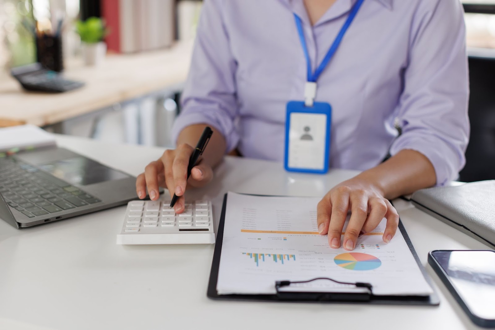 Closeup on a woman with a blue badge performing accounting services with a calculator and notepad.
