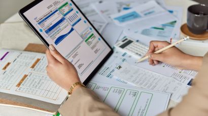 A bookkeeper cross-checking financial documents with tablet data while recording notes 