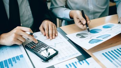 Two accounting professionals review company finances with a calculator and a chart