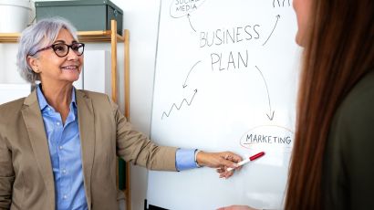 Senior business consultant reviewing a strategic business plan with a junior staff member during an in-office planning session.