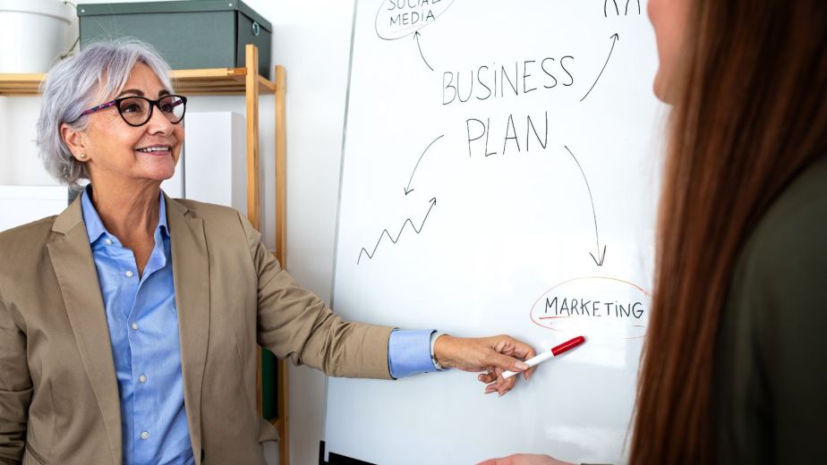 Senior business consultant reviewing a strategic business plan with a junior staff member during an in-office planning session.